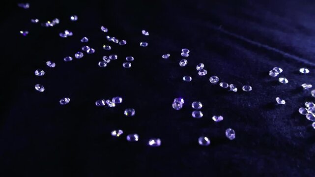 Multitude of small, brilliant cut diamonds are scattered across a soft, dark velvet surface, their facets catching the light and creating a beautiful, shimmering display of luxury and wealth