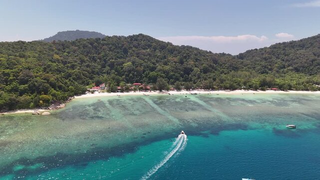 Cinematic 4K drone footage of a speedboat cutting through vivid turquoise waters as it arrives at the stunning Perhentian Islands, one of Malaysia's most idyllic tropical destinations, Terengganu.