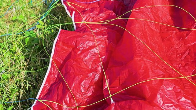 Macro shot of a red parachute canopy with thin green and blue lines on grass, highlighting paragliding setup, outdoor sport preparation, fabric detail, and adventure gear before launch.