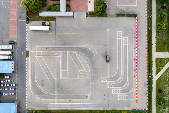 Aerial view of a driving school training course with white painted practice lines and a single car on an asphalt lot in Warsaw, Masovian Voivodeship, Poland.
