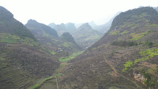 Aerial drone view of a sweeping limestone mountain valley with terraced farmland and rugged karst formations stretching across the Dong Van Karst Plateau in Ha Giang Vietnam