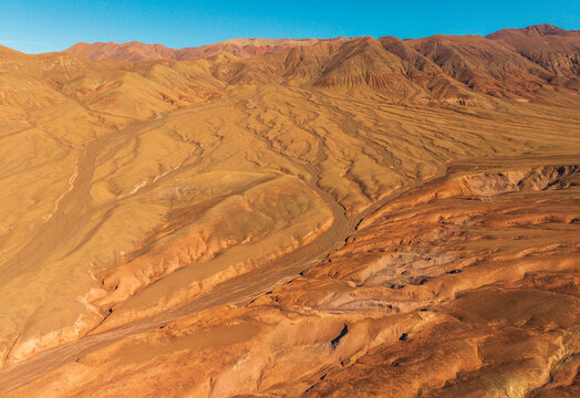 Aerial view of the arid desert landscape with undulating sand dunes and rugged mountain ridges under a clear blue sky in San Pedro de Atacama, Antofagasta, Chile.