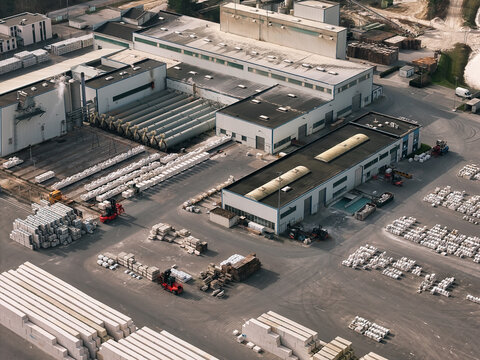 Aerial view of an industrial facility with warehouse buildings, rows of stacked construction materials, and forklifts in the yard in Dulmen, North Rhine-Westphalia, Germany.