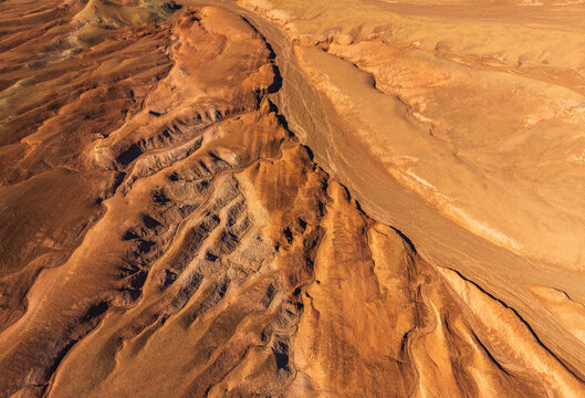 Aerial view of the rugged, arid landscape of the Atacama Desert with deep ravines, undulating sand dunes, and textured rock formations in San Pedro de Atacama, Antofagasta, Chile.