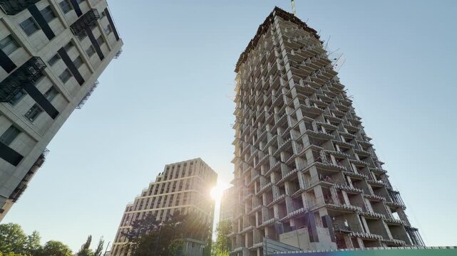 A massive concrete structure rises alongside modern buildings in Simferopol, Crimea. The warm sun casts an optimistic glow on the growing skyline, creating a feeling of vibrant progress and hope.