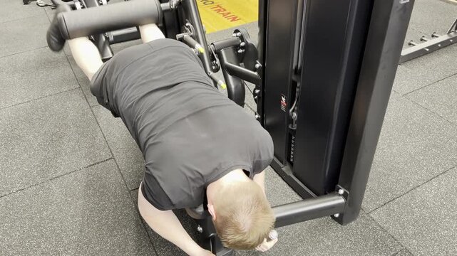 Man performing a prone leg curl on a gym machine, training hamstrings and lower-body strength during an indoor fitness workout