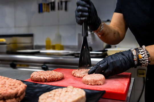 Chef pressing raw burger patties on a cutting board in a professional kitchen