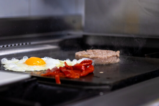 Cooking a gourmet burger with fried egg and roasted bell peppers on a hot griddle