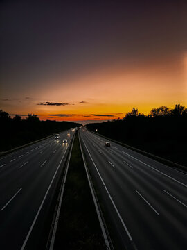 Aerial view of a highway at sunset with cars driving along the road under a vibrant orange and purple sky in Sehnde, Germany.