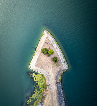 Aerial view of a triangular peninsula with sparse vegetation and a dirt path extending into deep blue water in Le Pouzin, Auvergne-Rhone-Alpes, France.