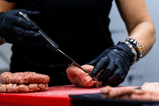 Chef hands in black gloves slicing fresh raw beef on a red cutting board