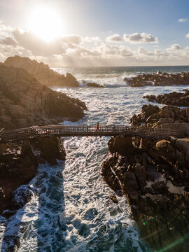 Aerial view of Canal Rocks Bridge spanning rugged rock formations with a person walking across, surrounded by crashing waves in Yallingup, Western Australia, Australia.