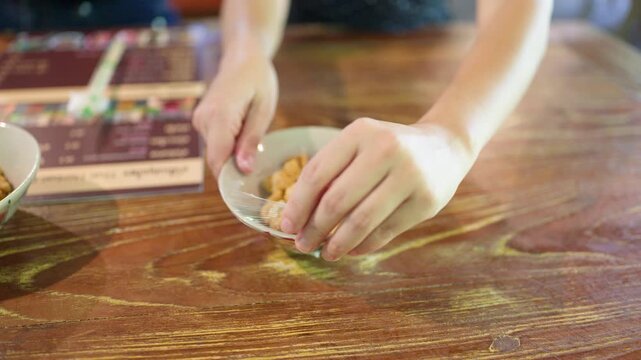 Hands Placing a Bowl of Crispy Pork Cracklings on Wooden Table