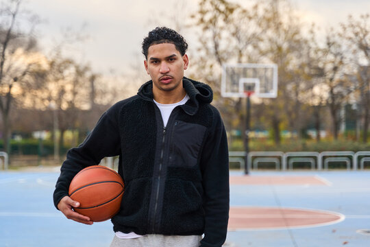 Young man holding basketball on urban court