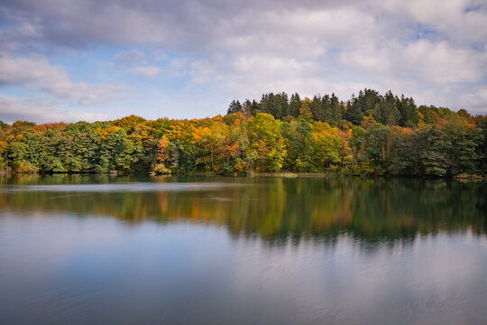 View of Velka Richnava Lake with vibrant autumn foliage and dense forest reflecting in the calm water in Stiavnicke Bane, Banska Bystrica Region, Slovakia.