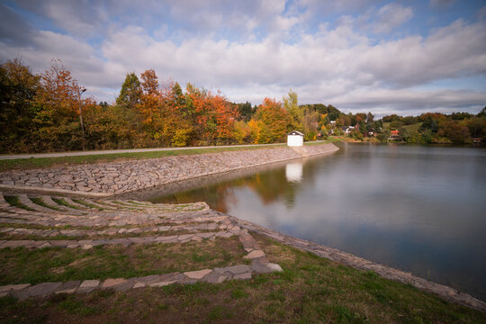 View of Velka Richnava lake with stone-paved embankments and autumn foliage under a cloudy sky in Stiavnicke Bane, Banska Bystrica Region, Slovakia.