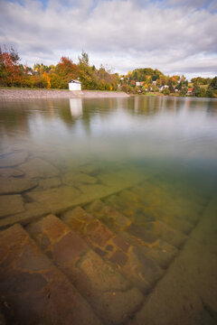 View of Velka Richnava lake with submerged stone steps, autumn foliage on the hills, and a small building on the bank in Stiavnicke Bane, Banska Bystrica Region, Slovakia.