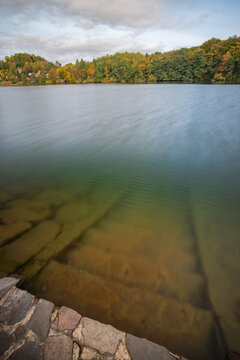 View of Velka Richnava Lake with stone steps leading into the calm water, surrounded by autumn foliage under a cloudy sky in Stiavnicke Bane, Banska Bystrica Region, Slovakia.