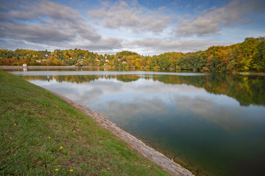 View of Velka Richnava Lake surrounded by autumn foliage and a stone embankment in Stiavnicke Bane, Banska Bystrica Region, Slovakia.