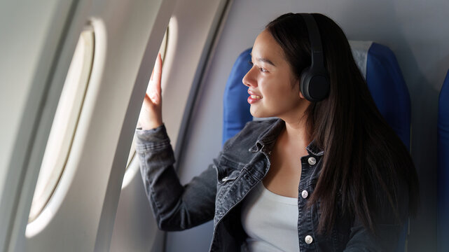 Asian woman with headphones looking out window of airplane during flight