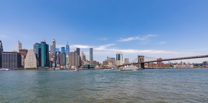 View of the Manhattan skyline and the Brooklyn Bridge over the East River under a clear blue sky in New York, New York, United States.