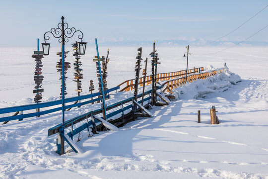 View of Goryachiye Istochniki Khakusy with wooden signposts and blue railing on a snowy pier overlooking frozen Lake Baikal in Severobaykal'skiy Rayon, Respublika Buryatiya, Russia.