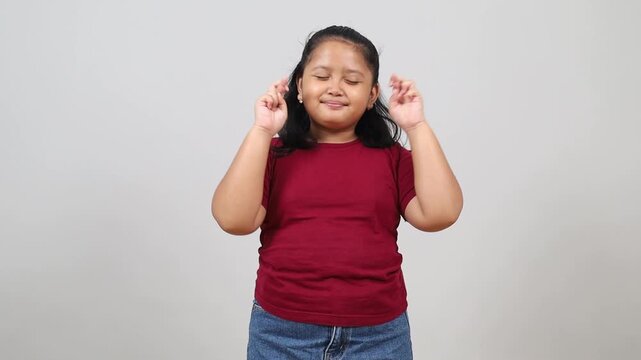 Asian little girl standing gesturing finger crossed smiling with hope and eyes closed. Luck and superstitious concept.