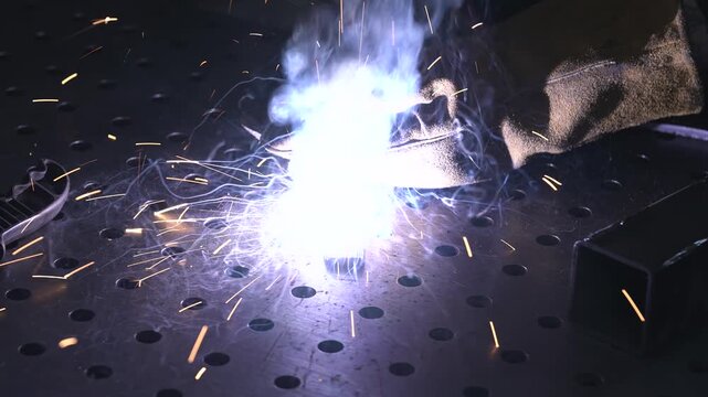 A working engineer welds metal parts with a manual welding machine