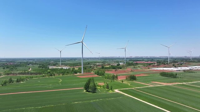 Multiple wind turbines stand tall across farmland plains under a clear blue sky