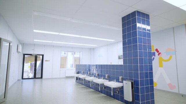 School hall contains handwashing zone with tiles and wall illustrations. Ceiling lamps create modern institutional atmosphere for children