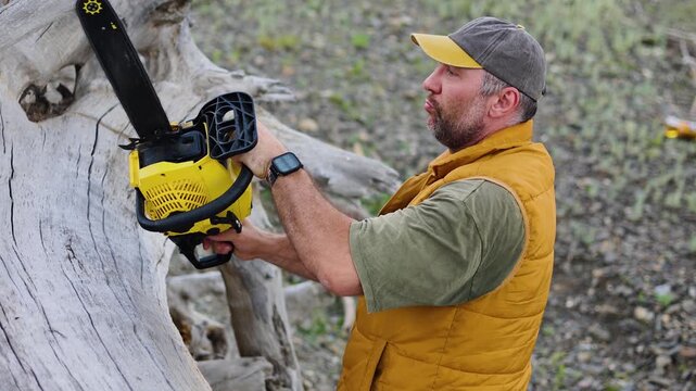 A diligent man starts his chainsaw and using a it to remove a fallen tree. Each cut brings him closer to a clean and safe landscape, reflecting dedication to outdoor tasks. Slow motion 4K footage.