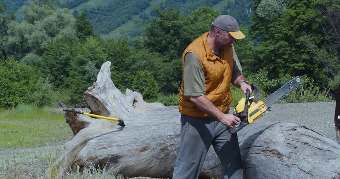 Slow motion 4K footage of a man starts his chainsaw and begins cutting down a tree felled by the hurricane. Hurricane cleanup and preparing firewood for the winter. Harvesting firewood for the winter.