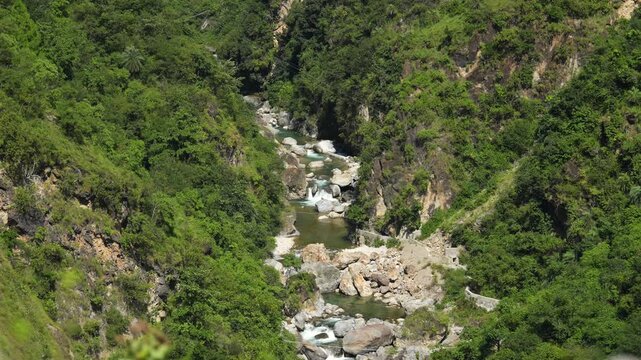 Natural landscape showing a wild rocky river valley and steep green hillsides on a bright day.