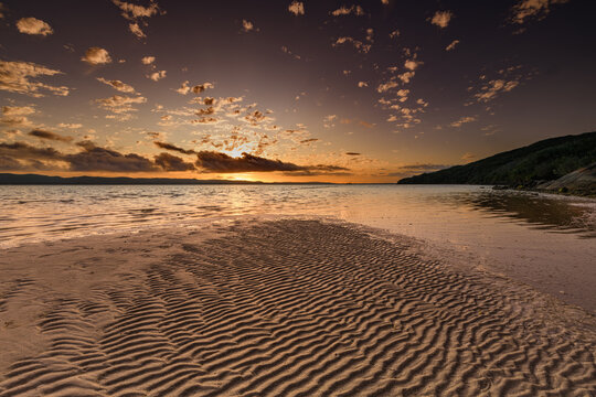 View of Quaranup Beach at sunset with rippled sand patterns, calm water, and a warm golden sky over the horizon in Vancouver Peninsula, Western Australia, Australia.