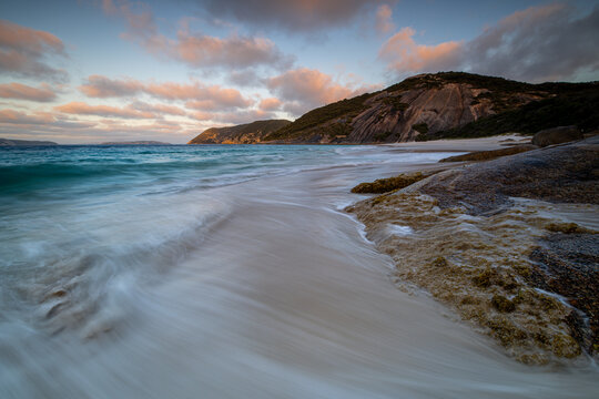 View of Misery Beach with waves washing over the white sand, rocky coastline, and soft sunset light in Torndirrup, Western Australia, Australia.