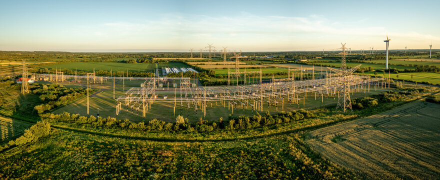 Panorama view of high-voltage electrical substation, transmission towers, power lines, wind turbines and battery energy storage system (BESS) installation. Concept of energy networks.