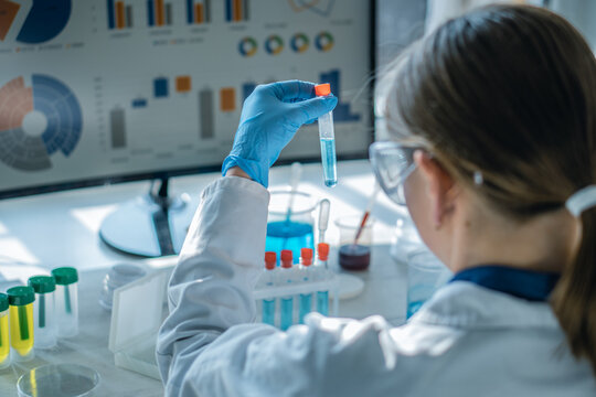 Female researcher conducts chemical experiment with blue liquid in test tube, focusing on scientific analysis. Laboratory environment features advanced technology and digital data visualization