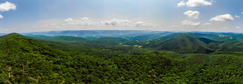 Lost City, West Virginia, United States - 12 June 2019: Aerial view of lush green forested mountains under a bright blue sky with scattered white clouds.