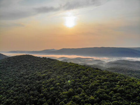 Lost City, West Virginia, United States - 12 June 2019: Aerial view of lush forested hills and valleys filled with morning fog under a soft sunrise sky.