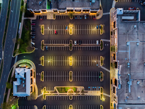 Reston, Virginia, United States - 12 April 2020: Aerial view of a commercial parking lot at dusk with illuminated street lights, marked spaces, and retail buildings.