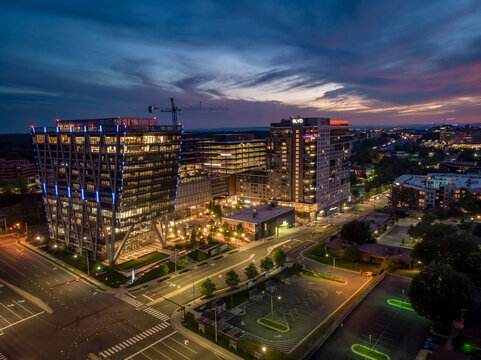 Reston, United States - 27 May 2020: Aerial view of modern office buildings and residential towers at twilight with illuminated windows and a construction crane.