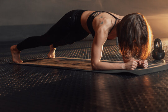A fit woman holds a plank position on a mat, emphasizing core stability and muscle engagement. The gym setting and kettlebell highlight a commitment to strength training and wellness