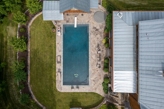 Harrisonburg, Virginia, United States - 09 August 2021: Aerial view of a rectangular swimming pool with a diving board, stone patio, and lawn next to a house.