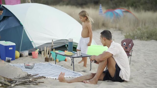 Young family with child spending quality time at beach campsite, sharing morning meal and laughter. Relaxed atmosphere, summer vibes, and outdoor adventure create unforgettable holiday memories