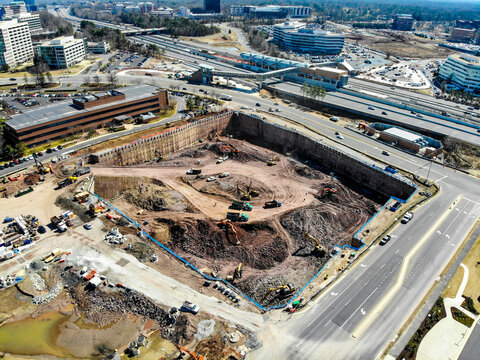 Reston, Virginia, United States - 12 March 2019: Aerial view of a construction site with heavy machinery, excavators, and trucks working in a deep excavation pit near a highway.