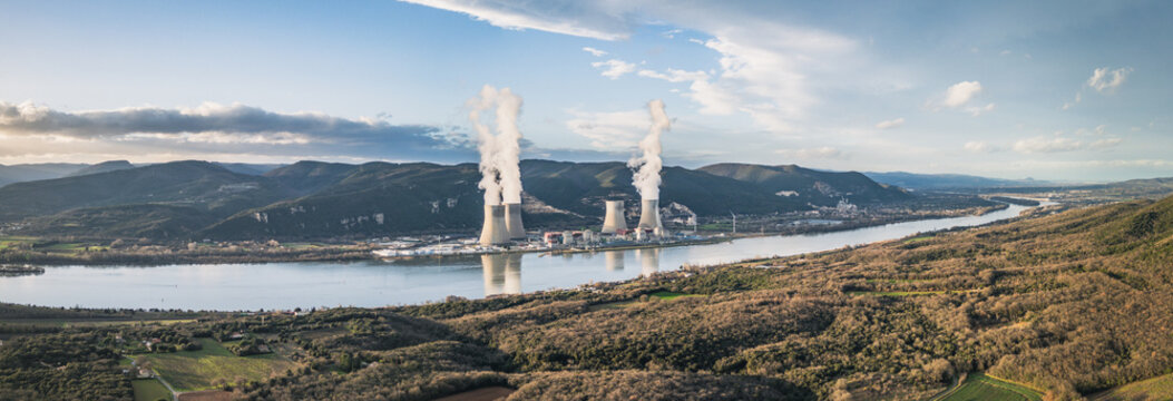 Cruas, France - 12 February 2026: Aerial view of the Cruas Nuclear Center with its cooling towers emitting steam, situated along the Rhone river amidst rolling hills and forests.