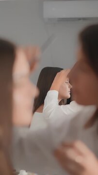 A focused makeup artist works on a young woman, creating a flawless look in a contemporary setting. The scene captures beauty, care, and the artistry of professional makeup application