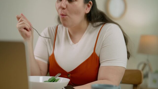 Plus Size Woman Checking Health Data on Smartphone and Laptop While Eating Salad