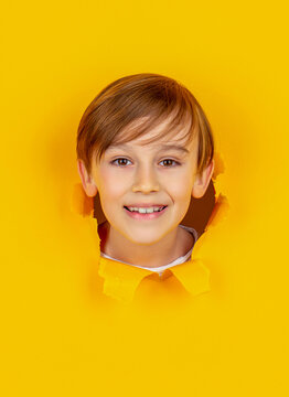 Breaking paper background. Emotions concept. Kid with toothy smile shows face in paper hole. Positive child with toothy pleasant smile on face