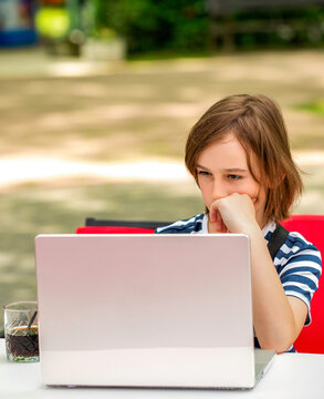Child boy studying. Schoolboy studying online on computer outdoors in park. Teen boy with a laptop sits behind a table in a park